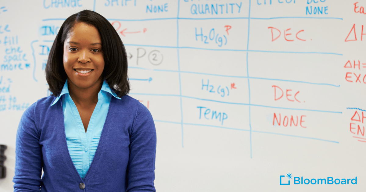 African American female teacher stands in front of whiteboard smiling at the camera.