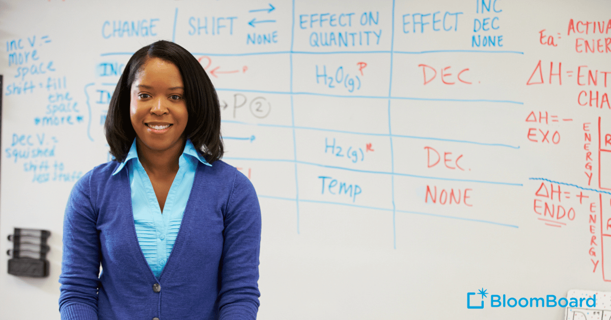 African American female teacher stands in front of whiteboard smiling at the camera.