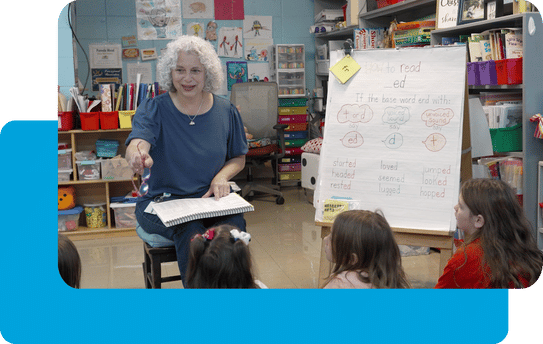 Teacher with gray hair leads a class of elementary school students.